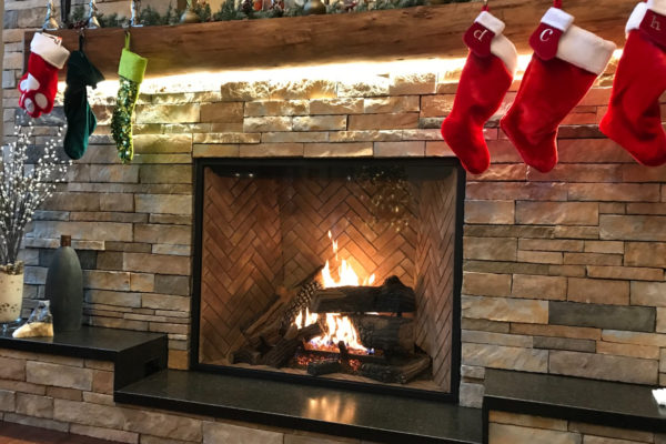 Festive Christmas stockings hanging over a stone fireplace with beautiful wood logs.