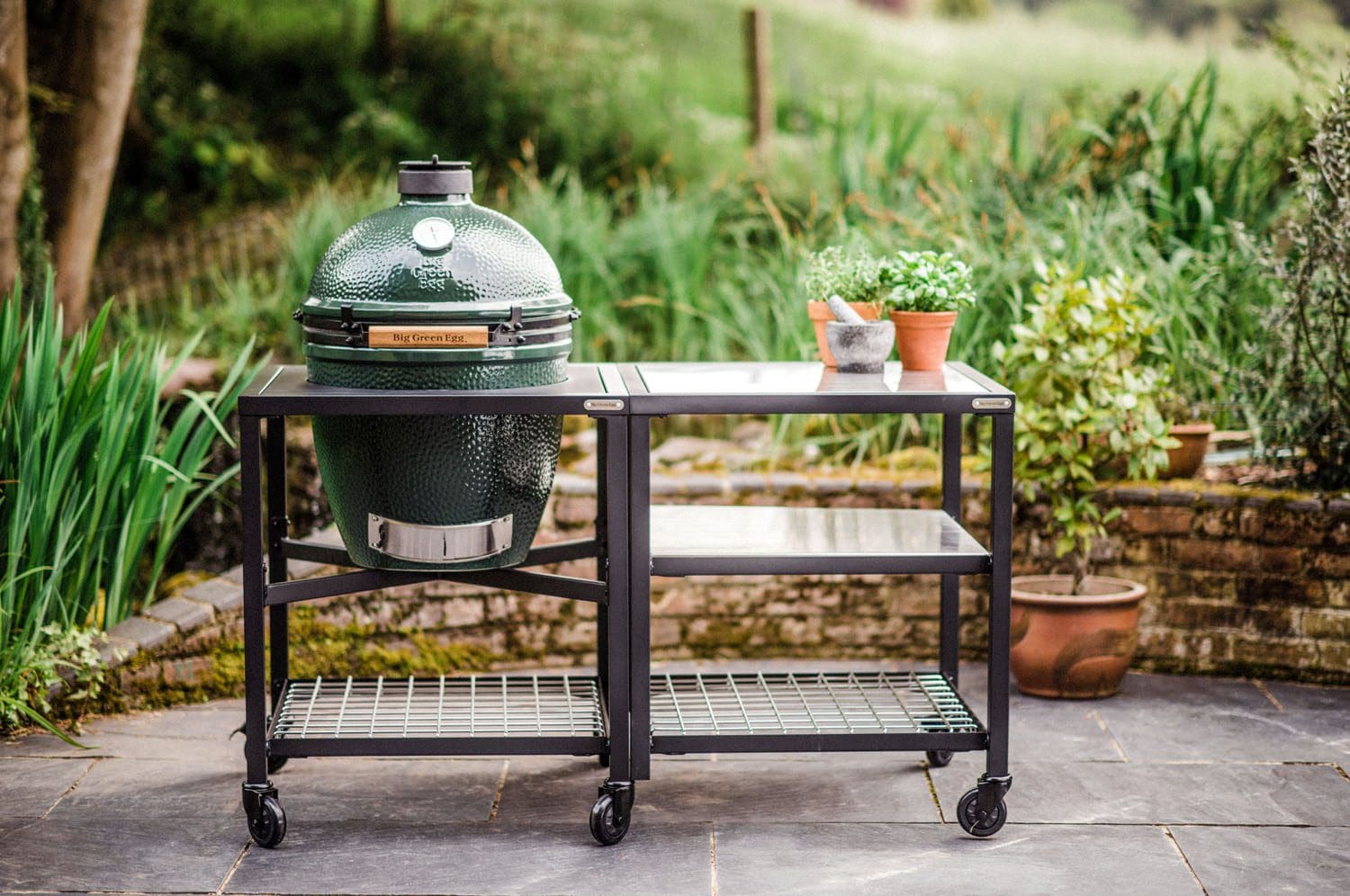 The Big Green Egg large ceramic smoker pictured in the modular nest in a beautiful patio garden.