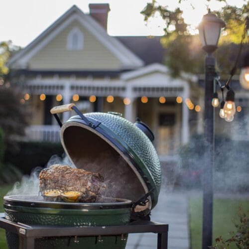 Meat smoking in the XL Big Green Egg outside a yellow home