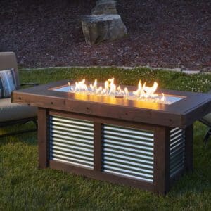 The Outdoor Greatroom Denali Rectangular Firepit is equipped with a rolling LP tank holder, glass burner cover, and a bottle opener.