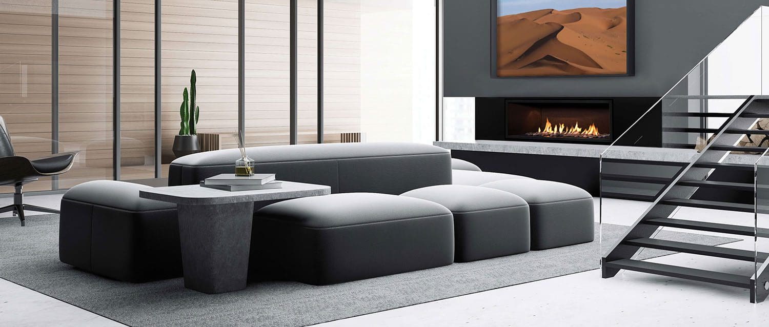 A modern living room with a black modular sofa, concrete coffee table, Mendota ML54 Linear gas fireplace glowing beneath a desert landscape photo, a cactus in the corner, and glass walls framed by wooden panels.