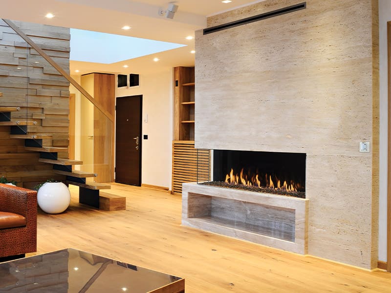 Modern living room featuring the Firenze™ Collection by DaVinci Custom Fireplaces™, wooden floors, an open staircase with glass railing, a textured wall, and recessed lighting for a warm, contemporary feel.